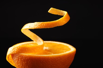 Photo of Fresh orange peel and half of fruit on black background, closeup