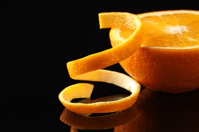 Photo of Fresh orange peel and half of fruit on black mirror surface, closeup. Space for text