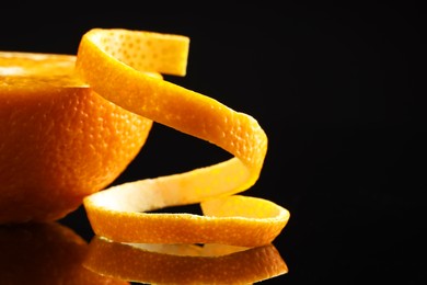 Photo of Fresh orange peel and half of fruit on black mirror surface, closeup. Space for text