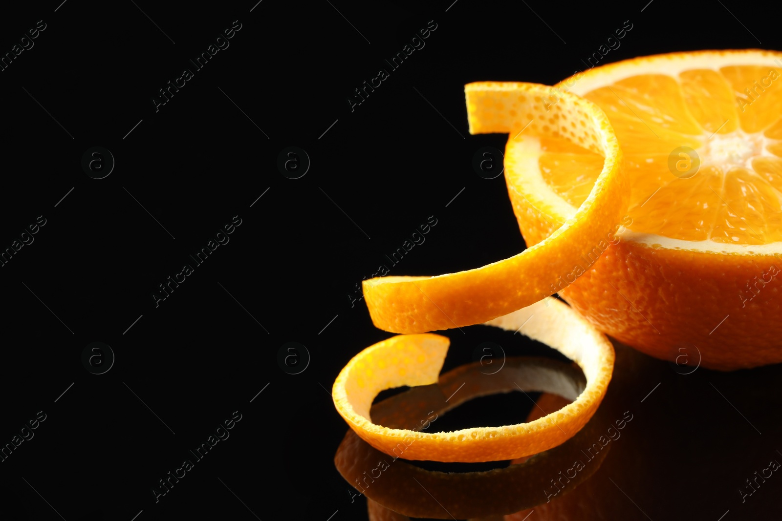 Photo of Fresh orange peel and half of fruit on black mirror surface, closeup. Space for text