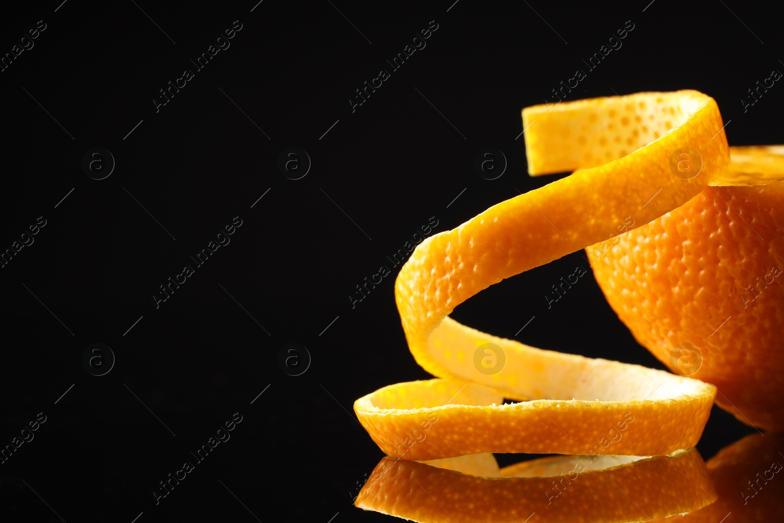 Photo of Fresh orange peel and half of fruit on black mirror surface, closeup. Space for text