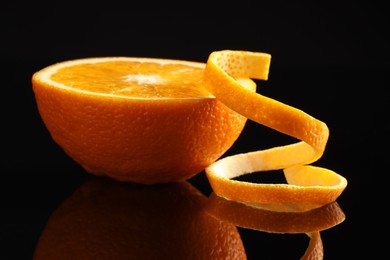 Photo of Fresh orange peel and half of fruit on black mirror surface, closeup