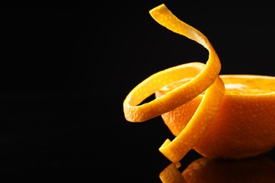 Photo of Fresh orange peel and half of fruit on black mirror surface, closeup. Space for text