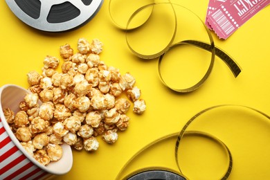 Photo of Movie tickets, sweet popcorn and film reels on yellow background, flat lay