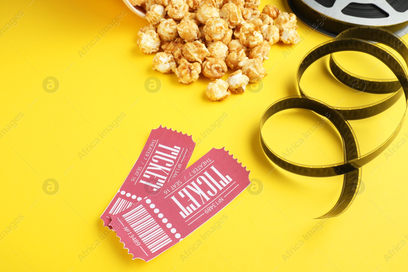 Photo of Movie tickets, sweet popcorn and film reel on yellow background, closeup