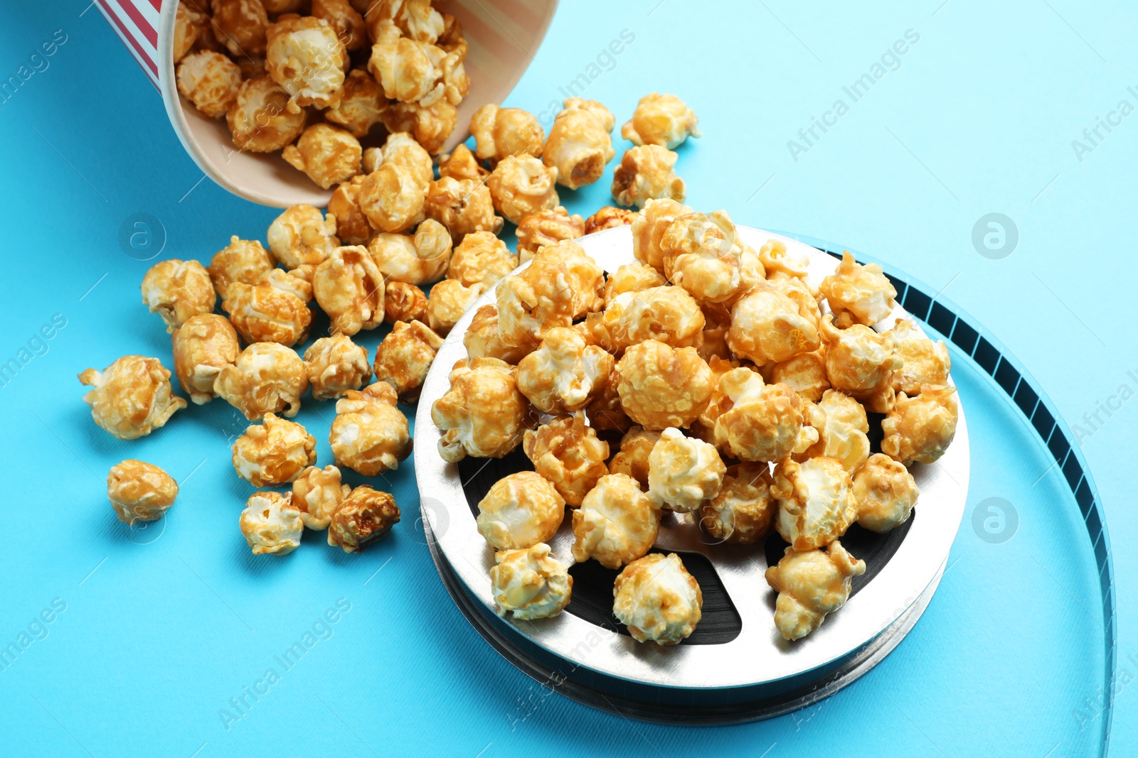 Photo of Sweet popcorn and film reel on light blue background, closeup. Watching movie