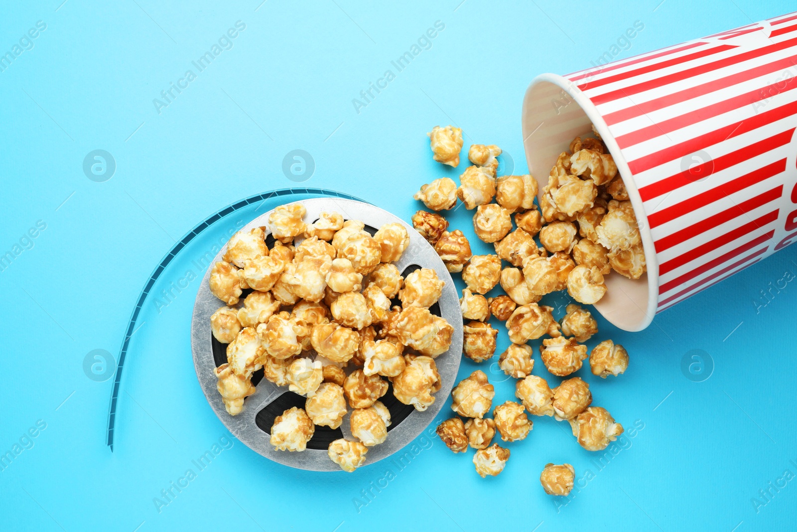 Photo of Sweet popcorn and film reel on light blue background, top view. Watching movie