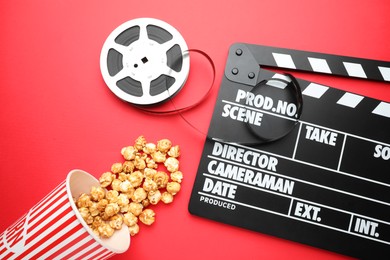 Photo of Movie clapper, sweet popcorn and film reel on red background, flat lay