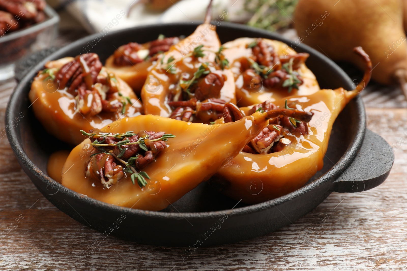 Photo of Delicious pears with caramel sauce, pecan nuts and thyme on wooden table, closeup