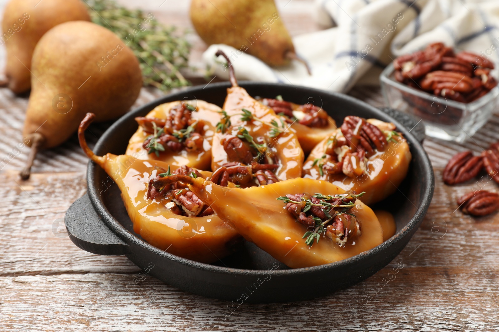 Photo of Delicious pears with caramel sauce, pecan nuts and thyme on wooden table, closeup