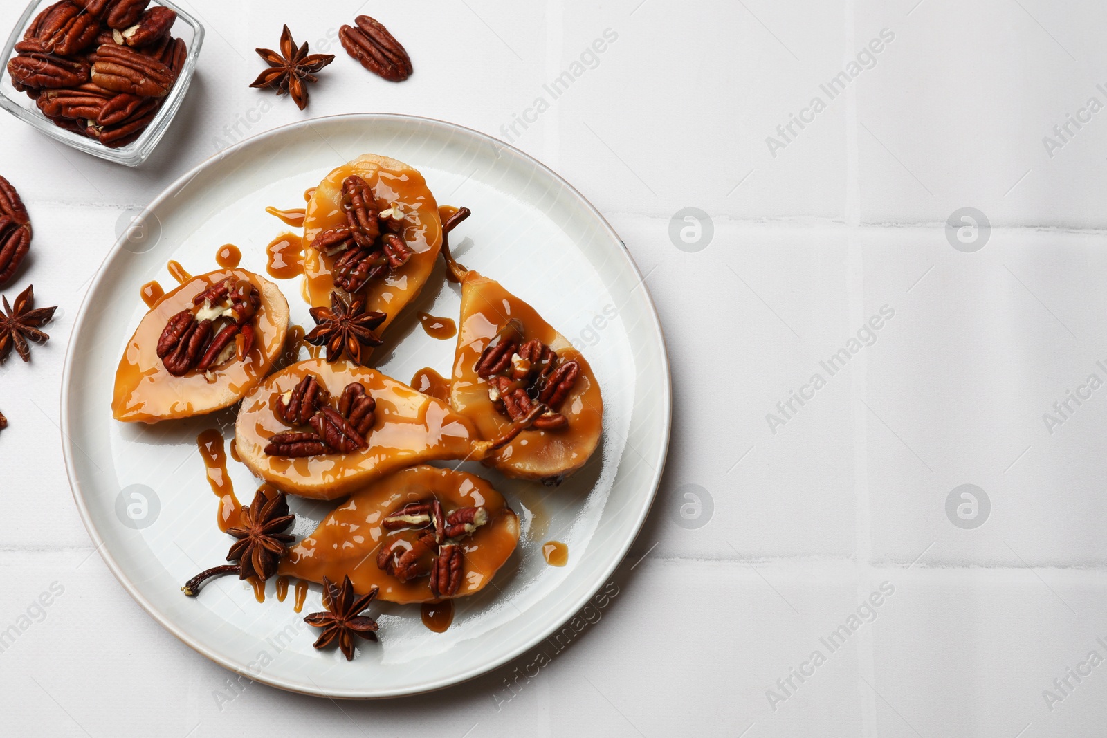 Photo of Delicious pears with caramel sauce, pecan nuts and anise stars on white tiled table, top view. Space for text