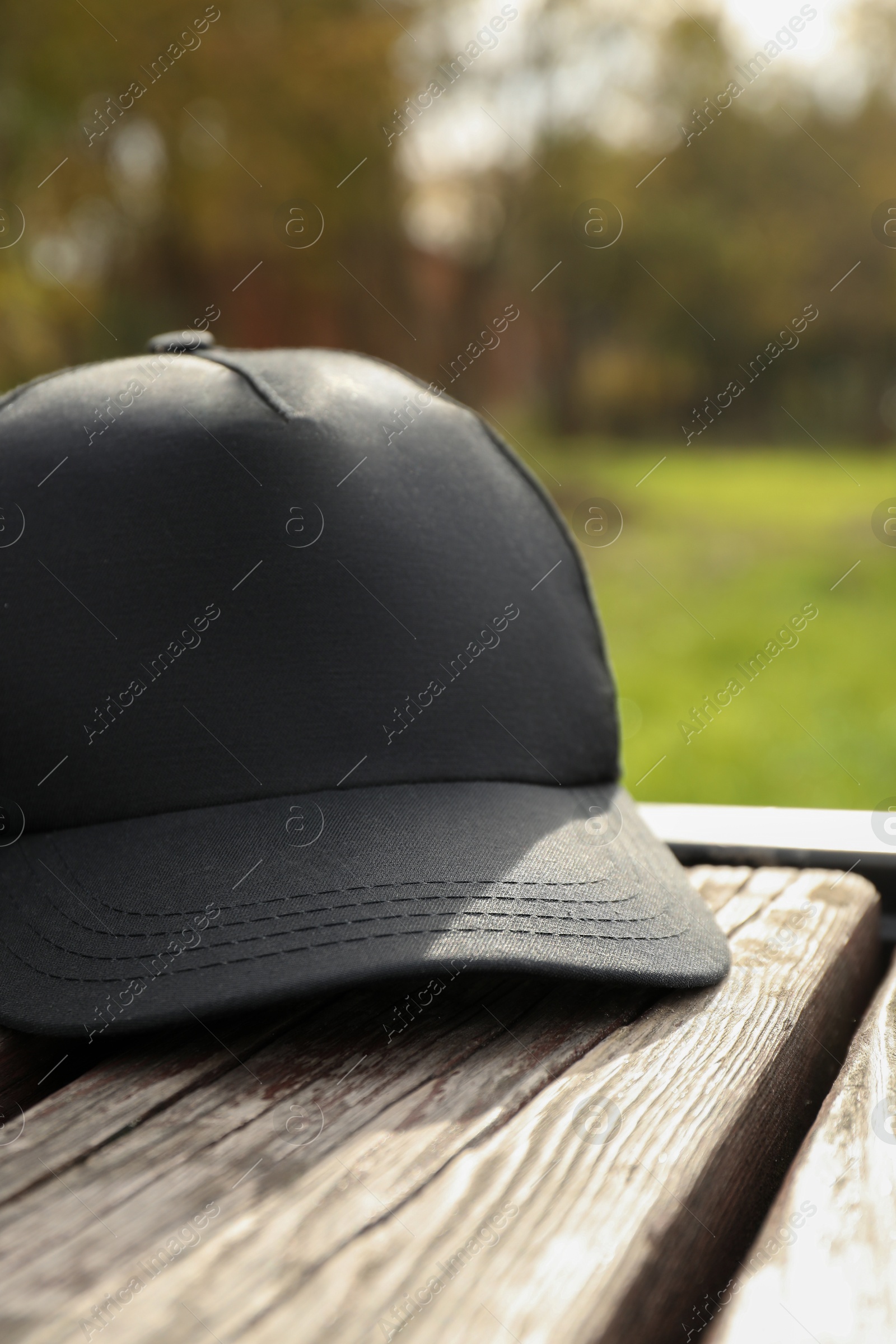 Photo of Stylish baseball cap on wooden bench in park, closeup. Mockup for design