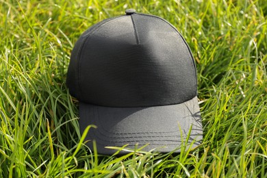 Photo of Stylish baseball cap on green grass, closeup. Mockup for design