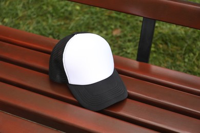 Photo of Stylish baseball cap on wooden bench in park. Mockup for design