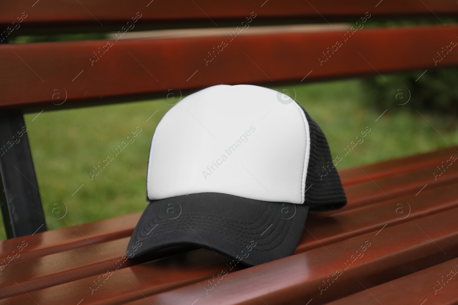 Photo of Stylish baseball cap on wooden bench in park. Mockup for design