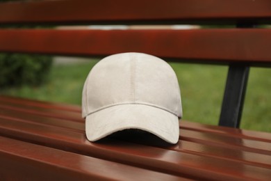 Photo of Stylish baseball cap on wooden bench in park. Mockup for design