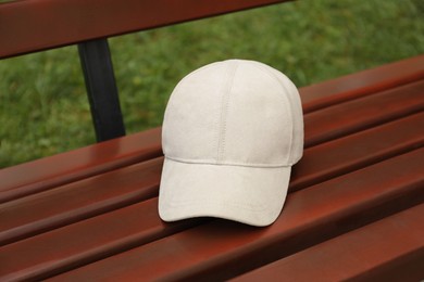 Photo of Stylish baseball cap on wooden bench in park. Mockup for design