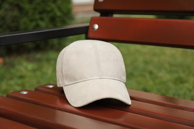 Photo of Stylish baseball cap on wooden bench in park. Mockup for design