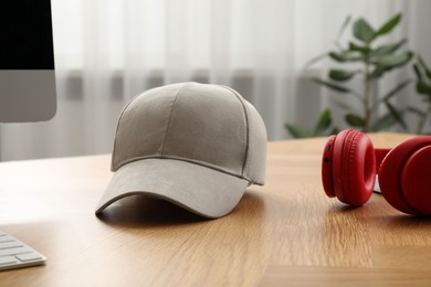 Photo of Stylish baseball cap on wooden desk indoors. Mockup for design