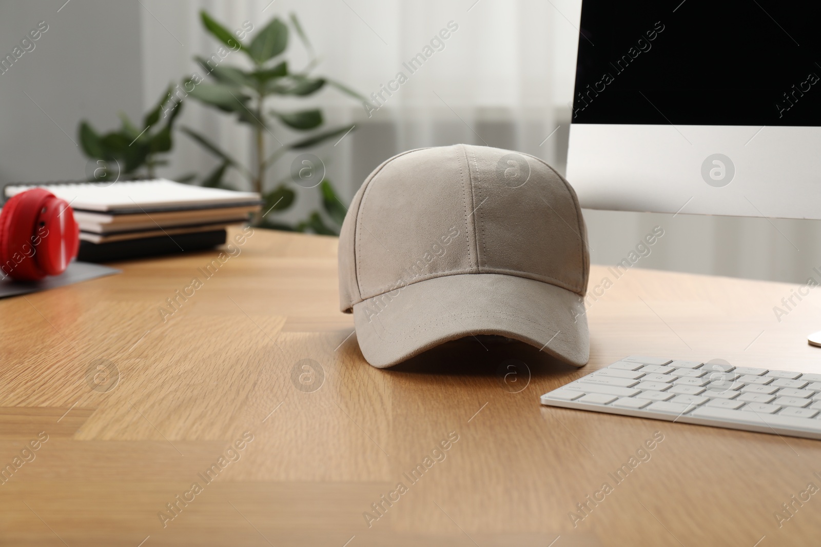 Photo of Stylish baseball cap on wooden desk indoors. Mockup for design