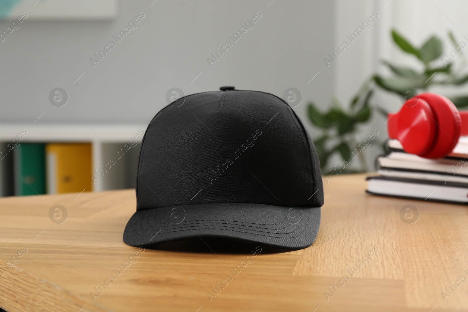 Photo of Stylish baseball cap on wooden desk indoors. Mockup for design