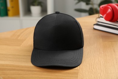 Photo of Stylish baseball cap on wooden desk indoors. Mockup for design