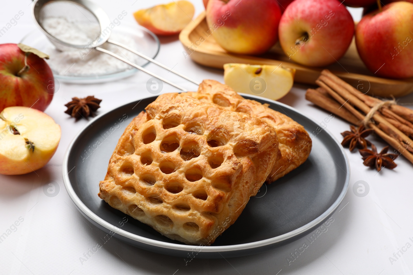 Photo of Delicious puff pastries, apples, cinnamon, anise stars and powdered sugar on white table, closeup