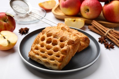 Photo of Delicious puff pastries, apples, cinnamon, anise stars and powdered sugar on white table, closeup