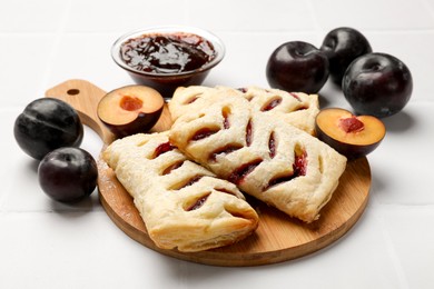 Photo of Delicious puff pastries, plums and jam on white table, closeup