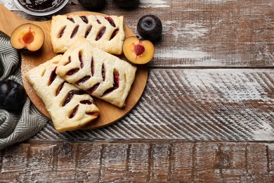 Photo of Delicious puff pastries and plums on wooden table, top view. Space for text