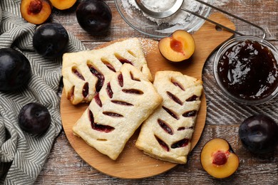 Photo of Delicious puff pastries, plums and jam on wooden table, top view