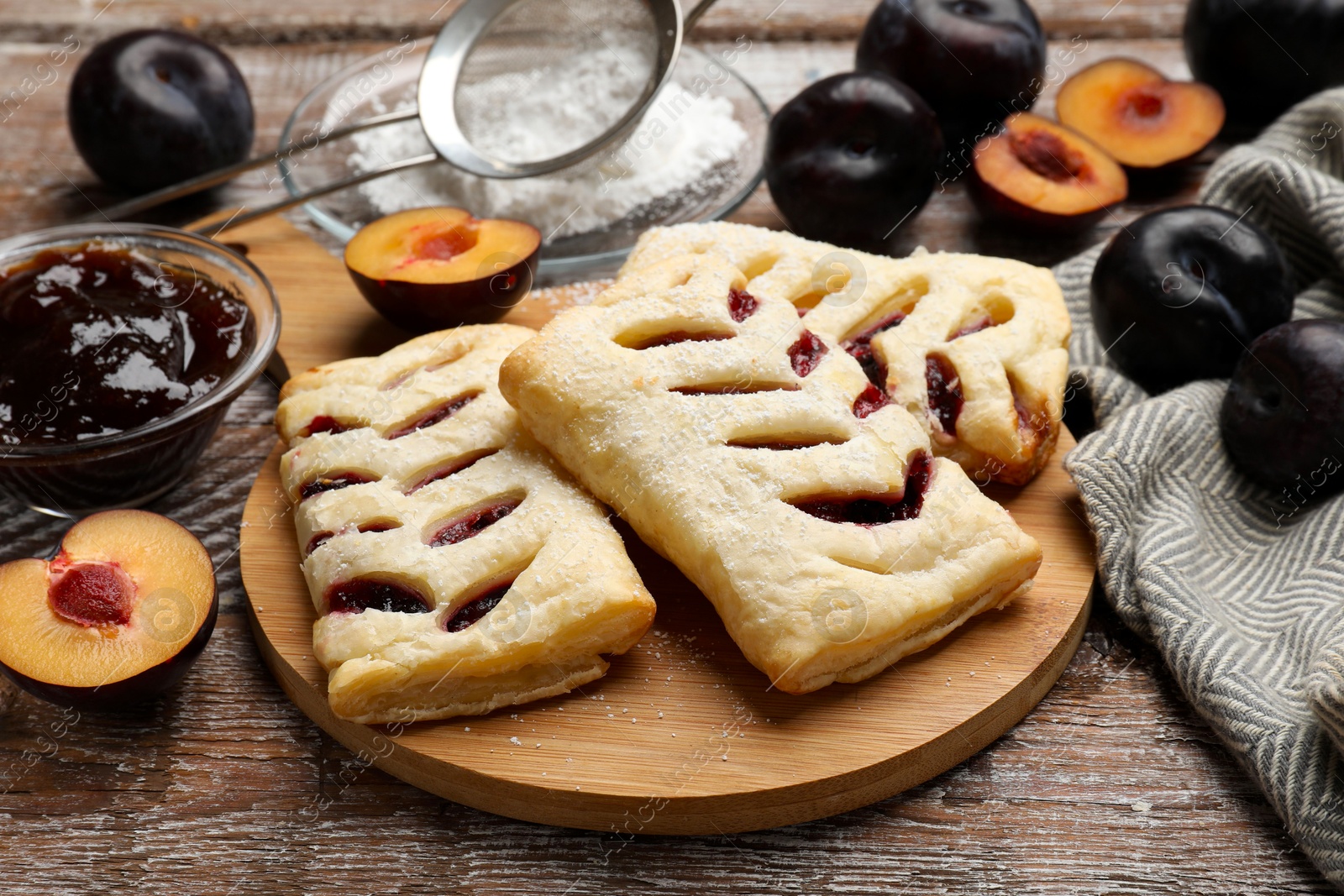 Photo of Delicious puff pastries, plums and jam on wooden table, closeup