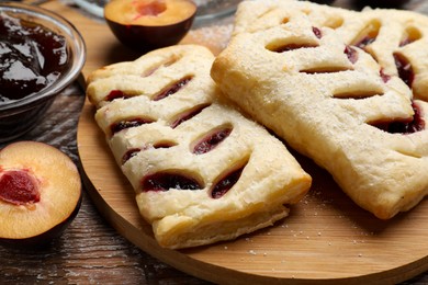 Photo of Delicious puff pastries, plums and jam on wooden table, closeup