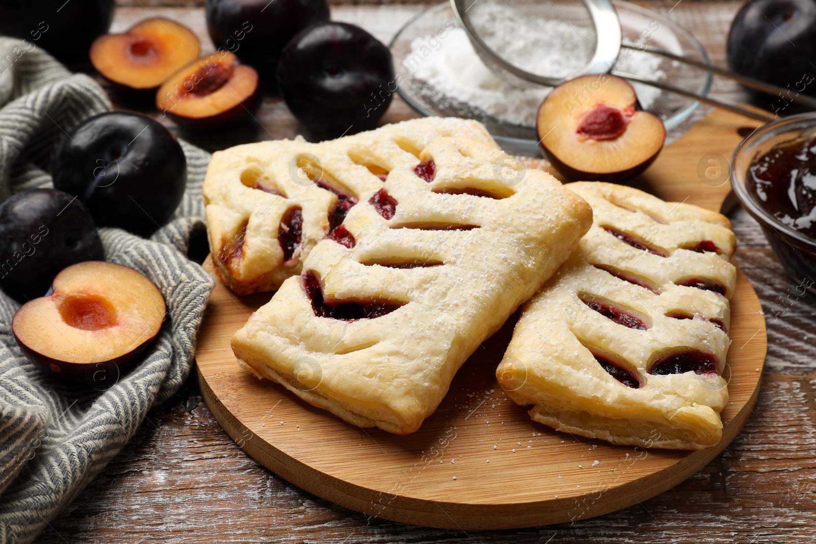 Photo of Delicious puff pastries and plums on wooden table, closeup