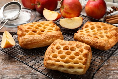 Photo of Delicious puff pastries with fruit filling and apples on wooden table, closeup