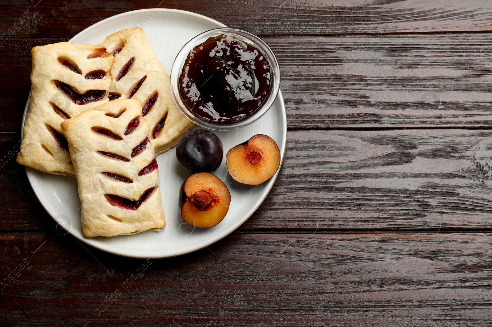 Photo of Delicious puff pastries, jam and plums on wooden table, top view. Space for text