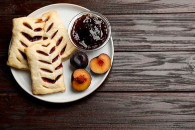 Delicious puff pastries, jam and plums on wooden table, top view. Space for text