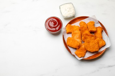 Photo of Tasty chicken nuggets and sauces on white marble table, top view. Space for text