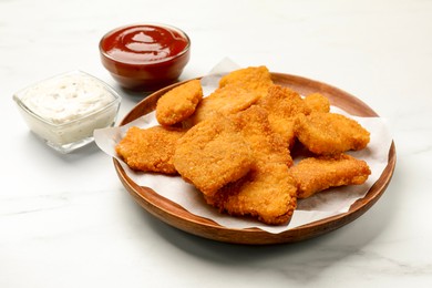 Photo of Tasty chicken nuggets and sauces on white marble table