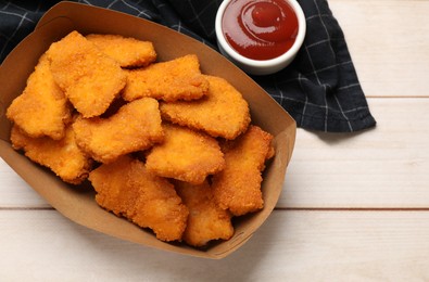 Photo of Tasty chicken nuggets in paper container and sauce on wooden table, top view