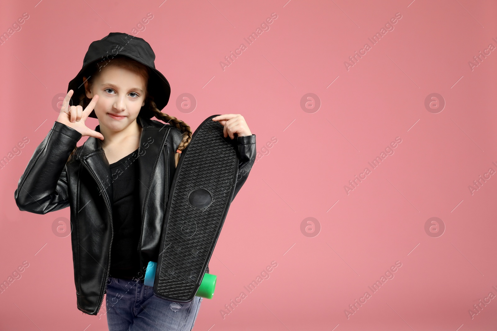 Photo of Little girl with penny board showing rock gesture on pink background, space for text