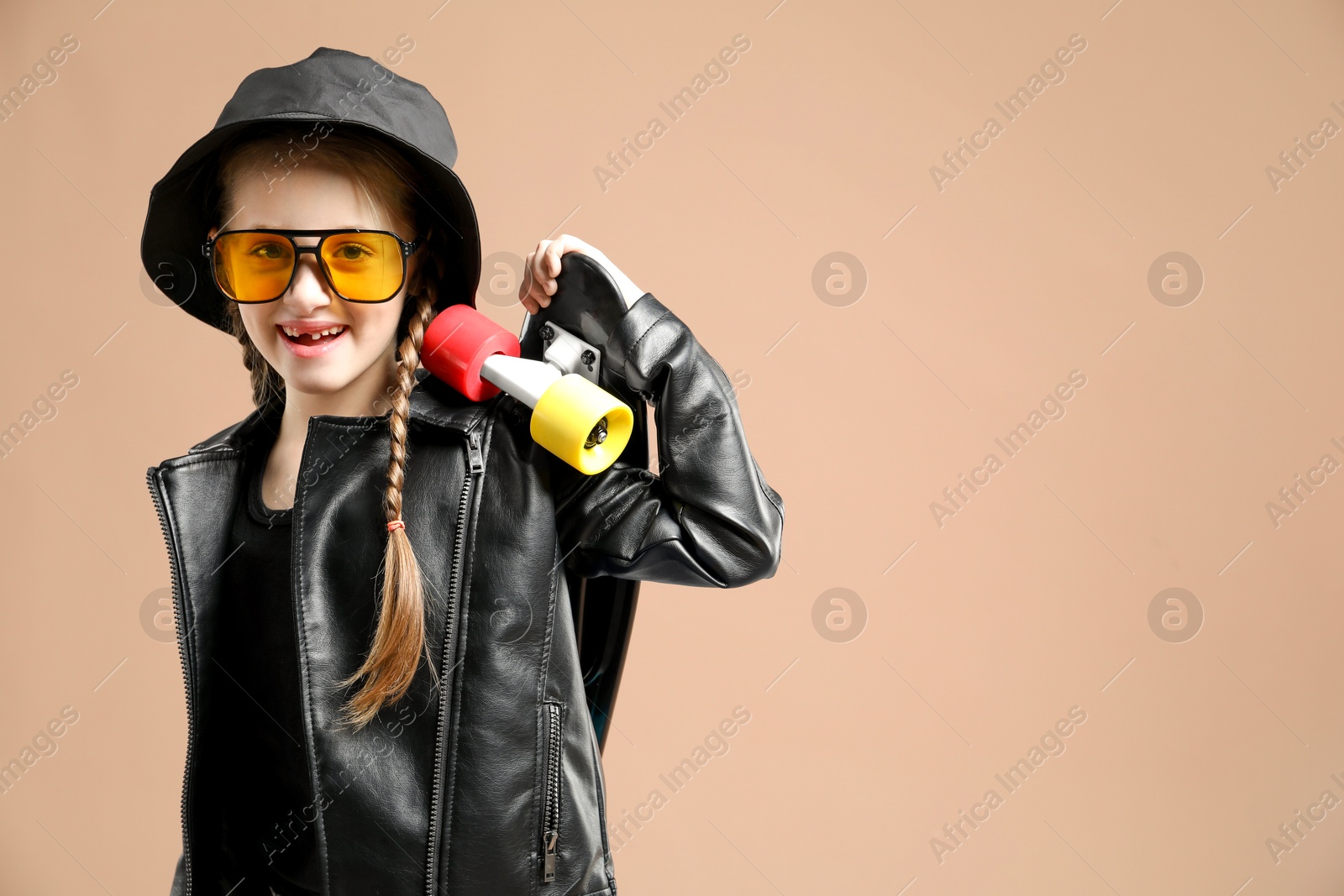 Photo of Little girl with penny board on pale brown background, space for text