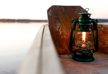 Photo of Vintage kerosene lamp in wooden boat near river at sunset