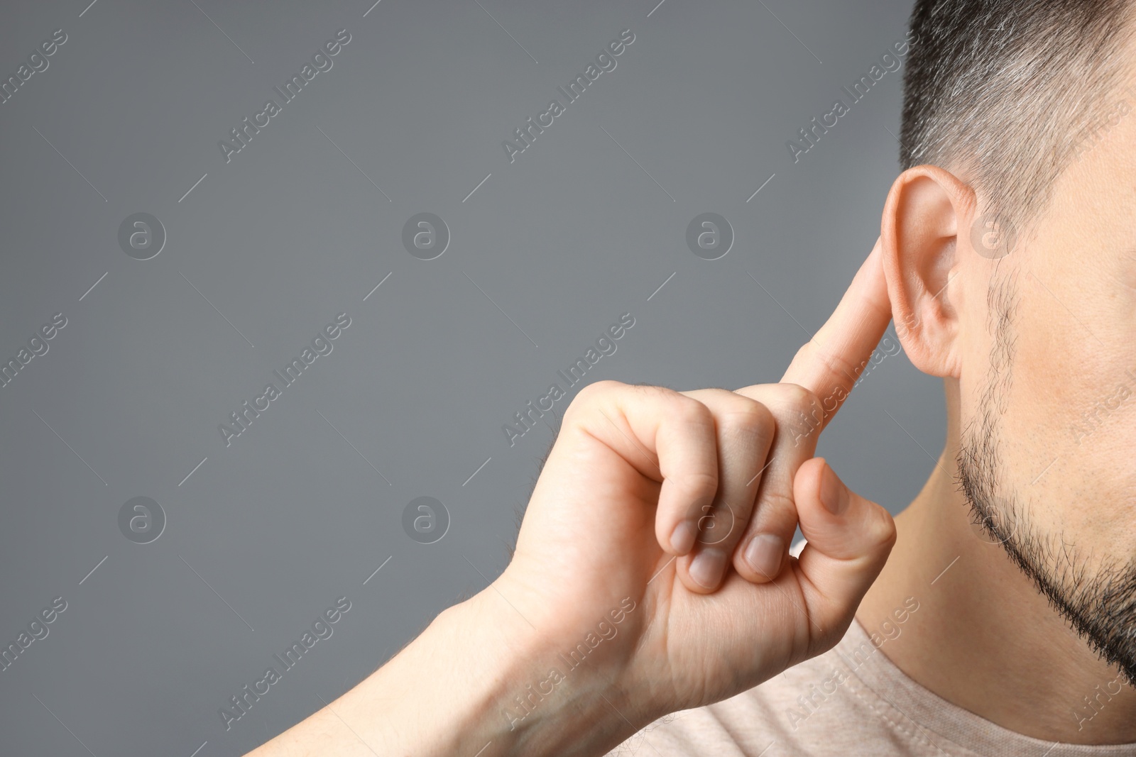 Photo of Man showing hand to ear gesture on grey background, closeup