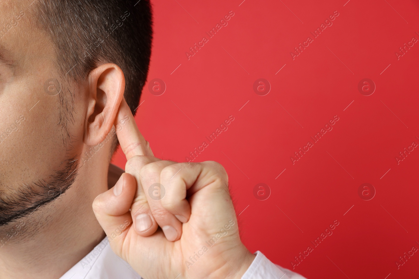 Photo of Man showing hand to ear gesture on red background, closeup. Space for text