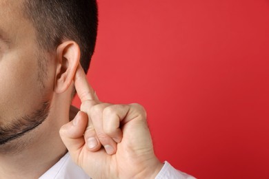 Photo of Man showing hand to ear gesture on red background, closeup. Space for text