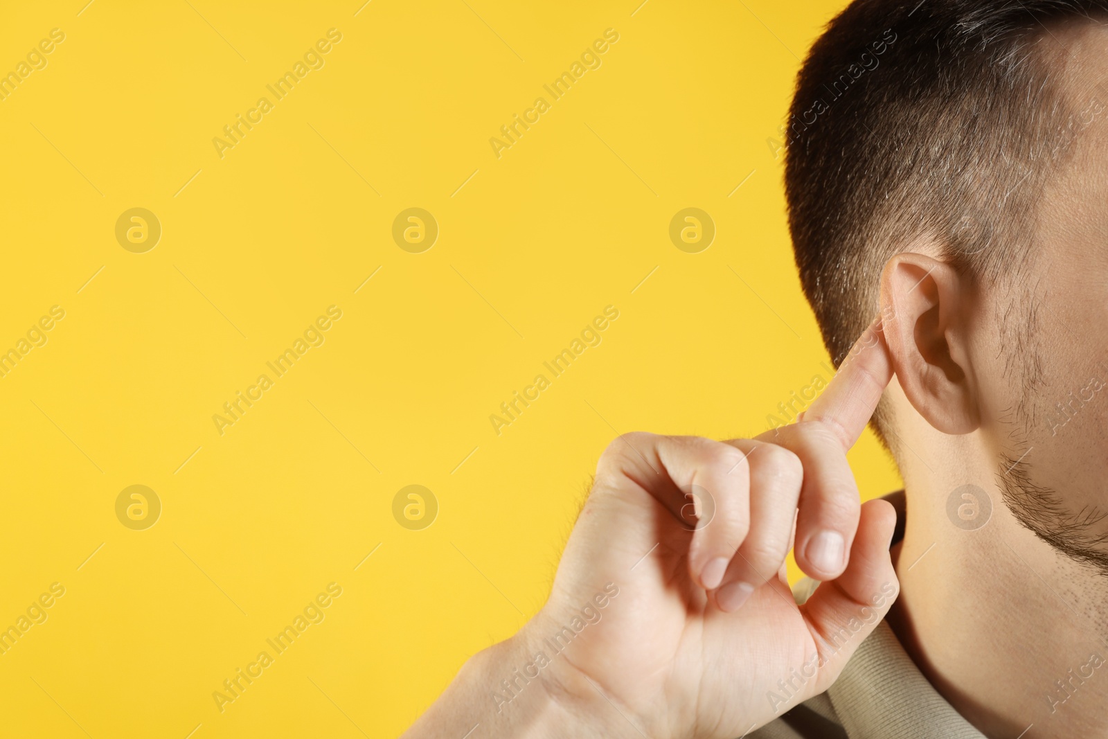 Photo of Man showing hand to ear gesture on orange background, closeup. Space for text