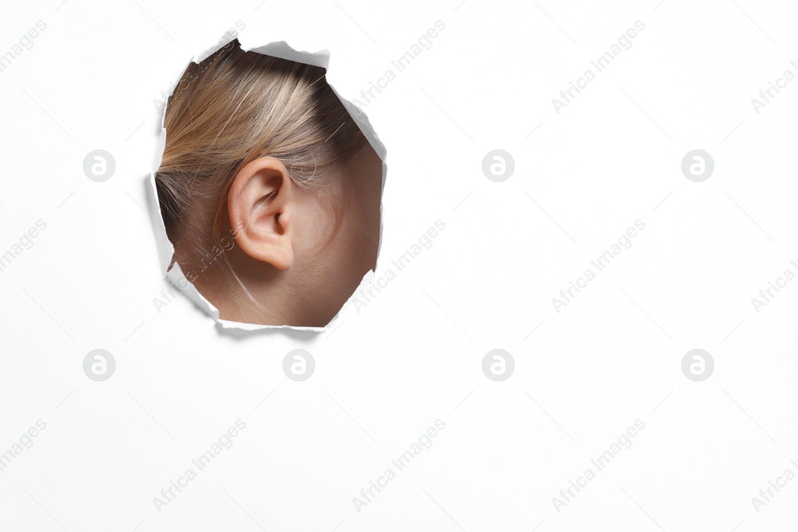 Photo of Little girl showing her ear through hole in white paper, closeup. Space for text