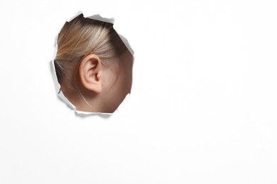 Photo of Little girl showing her ear through hole in white paper, closeup. Space for text