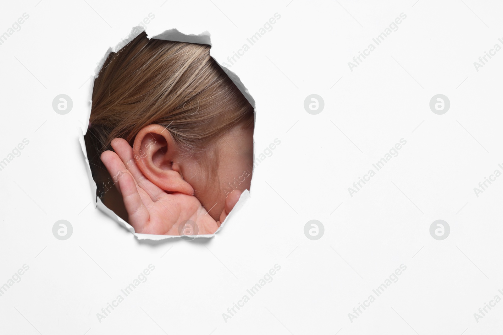 Photo of Little girl showing hand to ear gesture through hole in white paper, closeup. Space for text